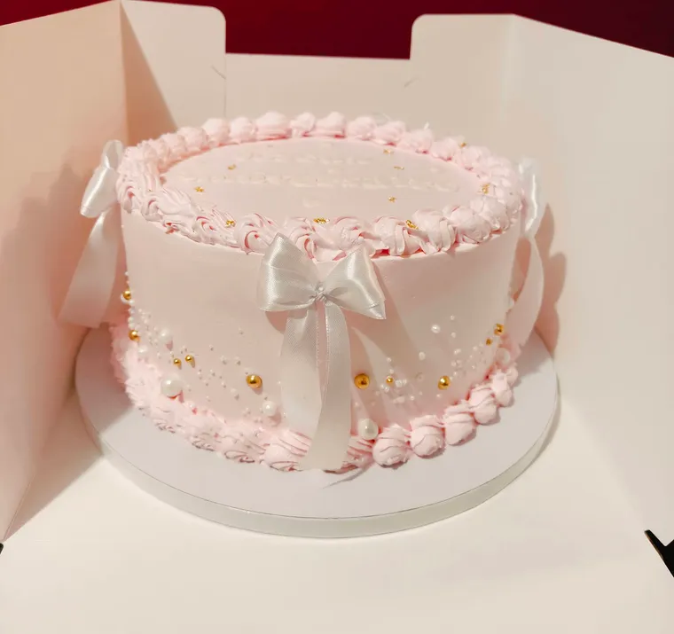 Gâteau rose pâle bordé de perles de crème, avec un nœud