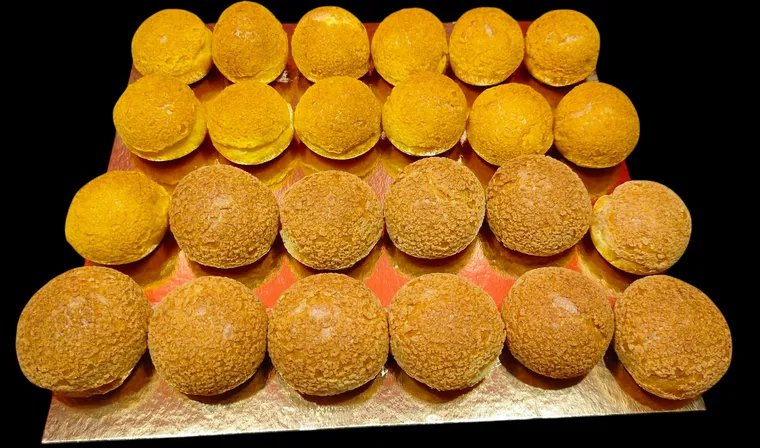 Mini-choux au craquelin dorés, alignés sur un carton doré
