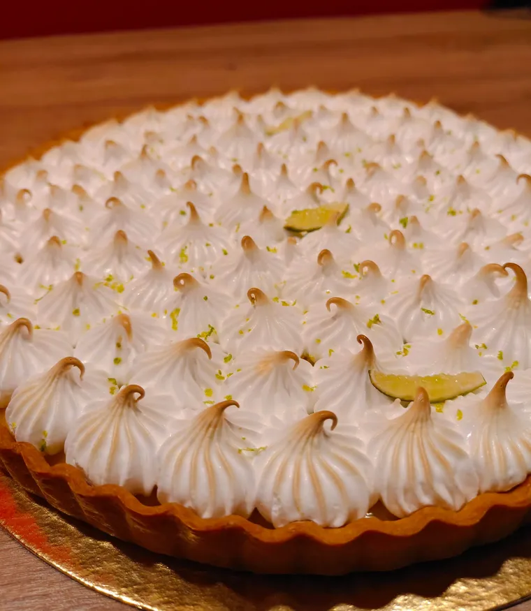 Tarte au citron meringuée, pointes de meringue dorées au chalumeau et zestes de citron vert